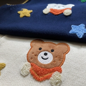 Close-up of bear embroidery and star patterns on premium knit sweater vests for boys