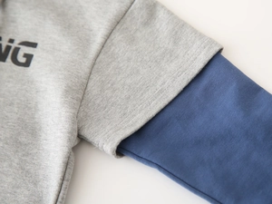 Detail view of children's grey hoodie sleeve with layered cuff design and NG print