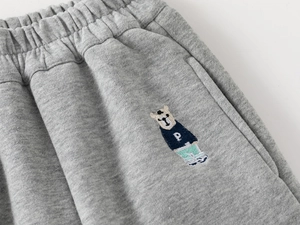 Detail of grey kid's jogger with elastic waist and bear embroidery in college style