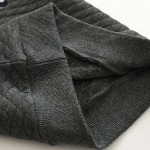Detailansicht des rautenförmig gesteppten grauen Stoffs und Rippbündchen am Kinderpullover