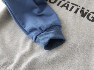 Close-up of ribbed cuffs and grey-blue spliced fabric on children's hooded sweatshirt