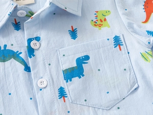 Dettaglio camicia azzurra a maniche corte con stampe di dinosauri e etichetta della taglia