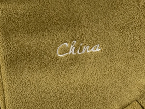 Close-up of olive green polar fleece fabric with white China embroidery detail