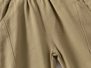 Detail of khaki kids trousers with elastic waistband, side pockets and vertical stitching