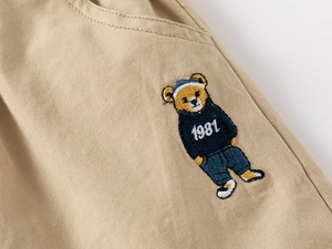 Dettaglio del ricamo a forma di orso e tessuto in twill di cotone su shorts kaki