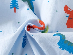 Dettaglio del tessuto in cotone azzurro con stampe di dinosauri e pini colorati