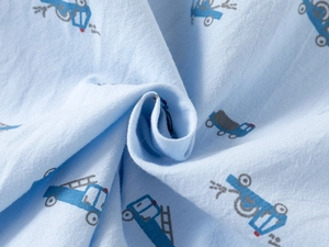 Close-up of soft light blue cotton fabric with colorful cartoon vehicle print details