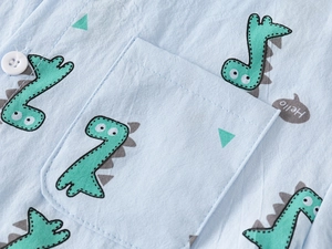 Close-up of light blue cotton shirt featuring green dinosaur prints and a small chest pocket