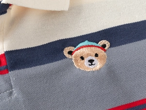 Détail d'un polo rayé pour enfant avec broderie d'ours et texture de coton piqué de qualité