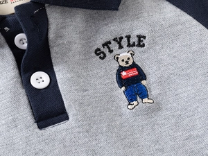 Detail of grey polo shirt with navy collar featuring teddy bear embroidery and buttons