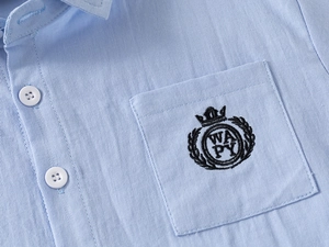 Detail of light blue boys shirt showing twill fabric texture and crown shield embroidery