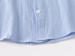 Detail of light blue cotton shirt featuring white button and neat hemline stitching