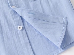 Close-up of boys' light blue shirt fabric texture with precise white button stitching details