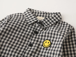 Detail of kids black and white plaid shirt with yellow smiley face embroidery and collar