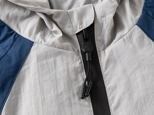 Detail shot of navy and gray windbreaker featuring a black resin zipper and hooded neckline