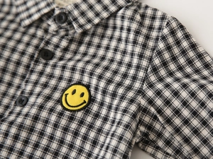 Detail of boys plaid shirt with black and white gingham pattern and yellow smiley face patch