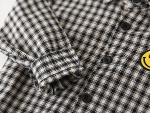 Close-up of black and white plaid kids shirt featuring a yellow smiley face embroidery