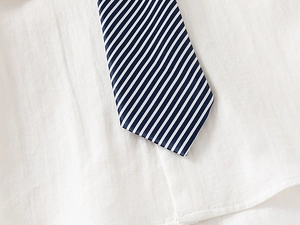 Détail d'une cravate rayée bleu marine sur une chemise blanche en coton pour garçon