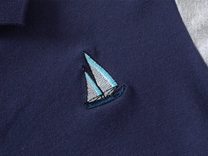 Dettaglio macro del tessuto polo piqué blu scuro con ricamo di barca a vela fine