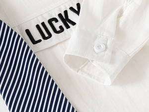 Détail de chemise blanche avec broderie Lucky et cravate à rayures bleu marine pour garçon