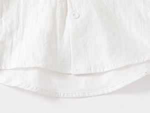Close-up of boys' white cotton shirt showing resin button and neat stitching on the curved hem