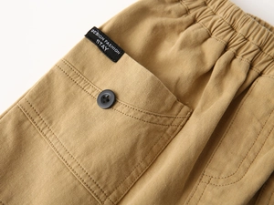 Detail of khaki cotton twill cargo pocket with button and fashion label on boys' shorts