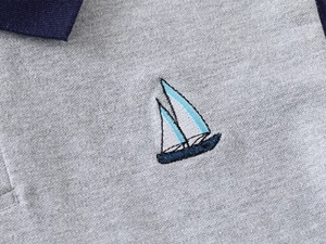 Dettaglio del ricamo a barca a vela e colletto blu navy su polo in cotone grigio
