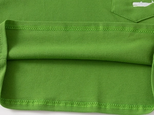 Detail of green piqué cotton shirt featuring whale embroidery and double-stitched hemline