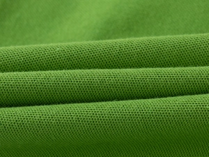 Close-up of grass green piqué cotton fabric showing breathable mesh texture for polo shirt