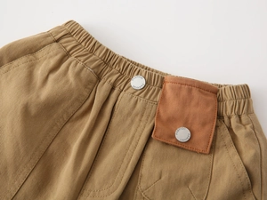Detail of boys' brown cotton shorts showing elastic waist and decorative pocket with buttons