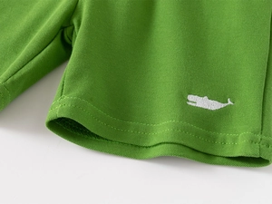 Detail of green piqué cotton shorts featuring high-quality white whale embroidery