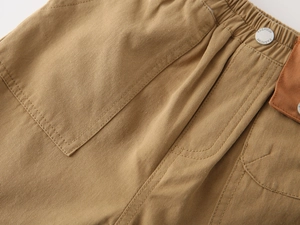 Detailed macro view of khaki cotton shorts featuring elastic waist and FASHION metal button