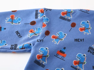 Detail of blue cotton knit fabric featuring cartoon dinosaur prints and fine stitching