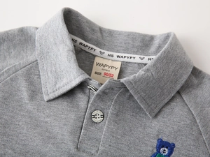 Détail d'un polo gris pour enfant montrant une broderie et la texture du tissu