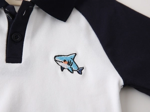 Detail of color-block cotton polo shirt featuring a small blue shark embroidery on chest