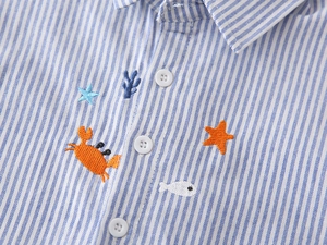 Détail d'une chemise en coton à rayures bleues avec broderie de crabe et d'animaux marins