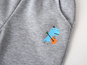 Detail of gray knit pants featuring a blue dinosaur graphic and neat side pocket stitching