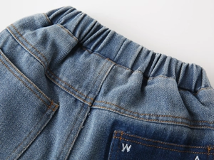 Detail of boys' denim jeans showing the elastic waistband and letter embroidery