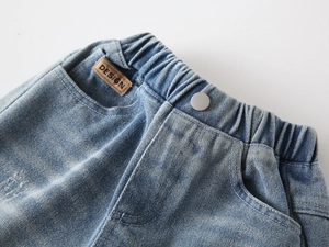 Detail of light blue kids jeans featuring elastic waistband and matte metal button