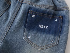 Detail of blue denim jeans back pocket with white embroidered letters and washed texture