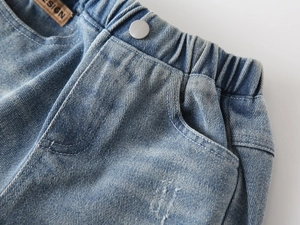 Macro view of blue denim jeans featuring elastic waistband and silver metal button detail