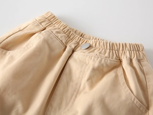 Detail view of children's cotton trousers featuring elastic waist with metal button and pockets