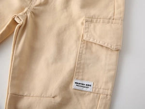 Detail of khaki cotton cargo pants for kids featuring side pocket and premium woven label