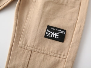 Detail of khaki cotton trousers showing a large cargo pocket with a black patch label