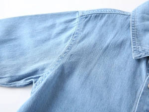 Detail of light blue denim shirt showing white contrast stitching and soft fabric texture