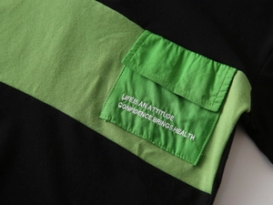 Macro detail of kids black and green polo shirt with utility pocket and embroidered slogan
