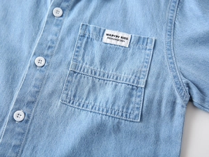 Detailed close-up of light blue kids denim shirt with chest pocket and white label
