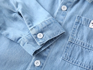 Detailed close-up of light blue denim shirt cuffs with white buttons and double stitching