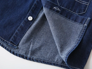 Detailed macro view of dark blue denim shirt hem showing white button and neat stitching