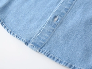 Detail of light blue denim shirt curved hem and precise stitching for boys' top